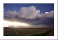 To the west, the sky is more docile with shallow cumulus clouds and a setting sun.