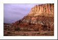 A brief glimpse of sunlight touches the red cliffs making them pop out against a mostly gray sky.