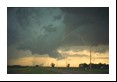 There are actually two tornadoes in this photograph. The first is quite near and has an obvious funnel; the second is at the end of the road as a swirling dust mass beneath a tilted rotating updraft cloud. The foreground tornado remained weak and moved south (left) while the background one grew bigger and moved northeast (right).